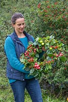 Woman holding an Autumnal Berry wreath featuring Wild Crab Apples, Hawthorn - Crataegus, Sloe berries - Prunus spinosa, Rose hips, English Oak - Quercus robur and Crocosmia seed heads
