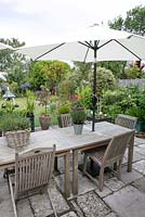 Wooden dining area on terrace. Salterns Cottage, a private garden on the Isle of Wight. 