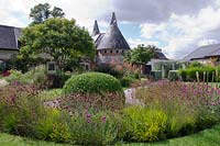 View of the Oast Houses with Koelreuteria paniculata tree and natural planting of  Dianthus carthusianorum, Digitalis ferruginea and Molinia grasses in foreground