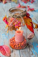 A glass jar candle holder decorated with autumnal foliage, Spindle and Pyracantha berries