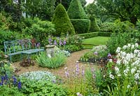 Formal garden with blue painted wrought iron bench, old sundial, gravel paths, roses, herbaceous perennials and view to lawns with box hedging and Yew topiary