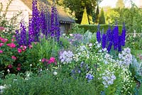 Shortly after dawn in the Sundial Garden at Wollerton Old Hall Garden, Shropshire - July. Planting includes David Austin roses, Delphiniums, Phlox paniculata and Campanula lactiflora. Beyond can be seen the pyramidal yews of the Yew Walk