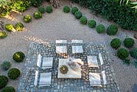 View of cobbled seating area and gravel garden with wooden sculpture in the sun and shadows. USA, August.
