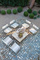View of cobbled seating area and gravel garden with wooden sculpture in the sun and shadows. USA, August.