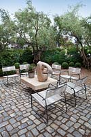 View of cobbled outside seating area with chairs and wooden sculpture with gravel garden beyond.