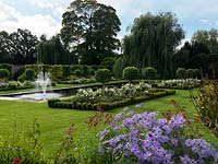 A formal garden with reflecting pool and fountain between box edged beds planted with Rosa 'White Flower Carpet' and evergreen Prunus lucitanica standards. In the foreground Penstemon 'Garnet', Aster frikartii and Salvia greggii 'Royal Bumble'.