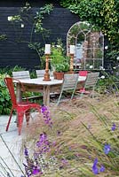 View through blurr of Erysimum 'Bowles Mauve' and Stipa arundinacea to dining table with pots of herbs.
