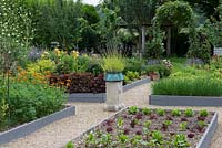 A potager with raised beds of chives and salad. A stone plith with a copper pot of  lavender provides a focal point on the central axis.