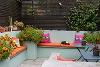 An outdoor room with built in benches and raised beds, planted with Gaillardia. Pet cat asleep 