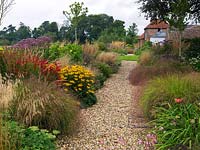A gravel path between double mixed borders planted with perennials and grasses including Geranium, Sedum, Helianthus, Crocosmia, Rudbeckia, Eupatorium and Stipa.
