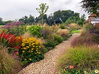 A gravel path between double mixed borders planted with perennials and grasses including Geranium, Sedum, Helianthus, Crocosmia, Rudbeckia, Eupatorium and Stipa.