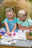 Two little girls, aged 6 and 9, pressing garden flowers in an old nursery rhyme book.