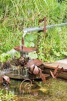 Water feature of lily flowers and pads made of rusted steel terraces causing water to cascade to pond. Jardin des Cimes Chamonix, July 