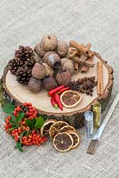 Creating a festive table decoration with dried fruit, nuts, seeds, with freshly picked berries and chilli peppers. Prepare with oak base, glue and glitter.