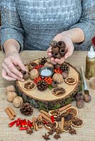 Creating a festive table decoration with dried fruit, nuts, seeds, with freshly picked berries and chilli peppers. Glue seed heads in place, continuing to work out from the centre.