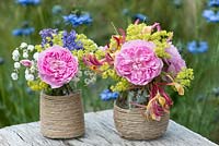 Colourful summer posies with pink rose, alchemilla, baby's breath, honeysuckle and catmint in glass jars decorated with twine.