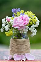 A colourful summer posie with pink rose, alchemilla, baby's breath and catmint in a glass jar decorated with twine.