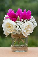 A summer posie with white roses, gypsophila and pink peony in a glass jar decorated with twine.
