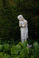 Stone statue of girl holding puppy underplanted with Bergenia - Elephant's ears