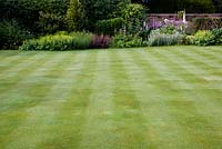Stripes on lawn in walled garden with mixed border behind.