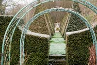 Rose arches frame a view along the garden's central axis flanked by clipped yew pyramids leading toward an obelisk at the far boundary
