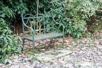 Green metal bench in a garden dusted with a light icing of snow. Dorset, UK