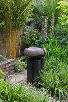 Seen over haze of fleabane, a ceramic bird bath by Sarah Walton in middle of corner courtyard.  To left, yellow bamboo, its stems stripped of leaves. Behind, Acanthus mollis.
