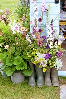 Cut flowers arranged in wellington boots against blue garden shed