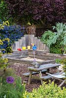 A sand pit and children's play area made from railway sleepers with floor covered with bark chippings. Behind, grey leaved cardoon, red leaved prunus and blue ceanothus.