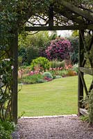 A view from beneath a rustic wooden arch  into a spring garden with camellia, tulips and ornamental grasses.