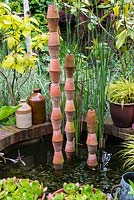 A small raised pond with stacked terracotta pots as a focal point.