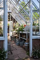 Aluminium greenhouse with work bench, watering cans and pot plants. Herrenmühle Bleichheim