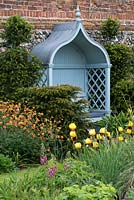 An arbour, edged in yew hedges and Geum 'Totally Tangerine', overlooks border with Iris 'Rajah'