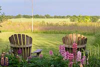 Behind a border of lupins, two ariondack chairs look out accross the meadow and Essex countryside beyond.
