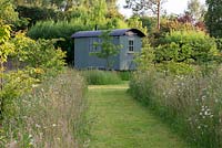 A grass path mown though a meadow with grass and ox-eye daisies leading to a shepherds hut.