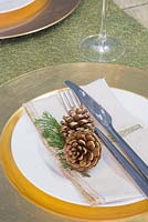 A festive place setting featuring a gold plate with Pine cones and foliage