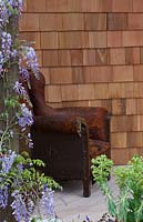 Wisteria sinensis growing up a recycled timber post next to a rustic leather armchair.