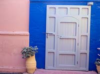City housefront - green door in blue wall, pelargonium in tall yellow pot