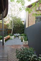 View from timber decking in inner city courtyard to lower level with small dining area and back fence covered with Phylostachys nigra, black bamboo. Bench and concrete planters with various shade loving plants