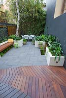 View from timber decking to lower area of inner city courtyard with small dining area and back fence covered with Phylostachys nigra, black bamboo. Concrete planters with various shade loving plants