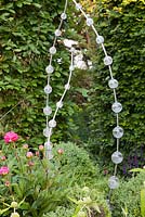 Decorative metal and glass sculpture Plume by Loco Glass amongst Buxus balls and Peonies in border