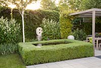 Clipped box hedge around Infinity pool on patio with contemporary statue 'Untitled' by artist Will Spankie, white Astilbe and covered seating area for entertaining 