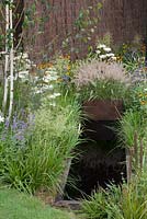 Harsh diagonal waterways populated with Eriophorum vaginatum planters representing cotton crops arriving into Manchester via the Bridgewater canal in the 'Black Pepper' Garden at RHS Tatton Flower Show 2015
