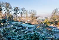 View of the glasshouse and rock garden with ground covering conifer Picea mariana 'Nana' -AGM - dwarf black spruce in the foreground, RHS Garden Wisley, Surrey 