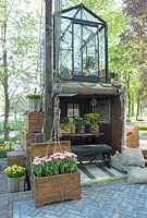 Greenhouse on top of a container. Tiny house in container with classic old aged furniture and pictures. Wooden boxes filled with Narcissus and Hyancinthus. Wooden stair to top. Inspiration garden: Golden Age.