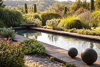 Modern pool edged with stone slabs and surrounded by mediterranean style planting - July, Les Jardins de la Poterie Hillen
