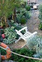 Beach themed garden with rope, life belt, white painted seat, crab nets, buoy, crambe maritima, gravel, agave, artemisia and tamarix. 
