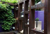 Heavy rail sleeper loggia garden divider with candle holders and other decorative items on shelves. Aluminium planter and perspex sheet fence in background. Wisteria. 