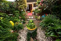 View from back fence to rear of house in inner city garden features mondo grass, bromeliads and strappy leafed plants, as well as colourful eclectic retro pieces sourced from local markets. 