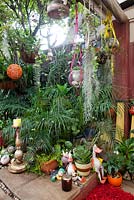 A collection of quirky statues, seabird statues, palms, Spanish Moss, Tillandsia usneoides, succulents, orange plastic lampshade and a birdhouse.